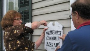 Two people removing original brunswick library sign from old building